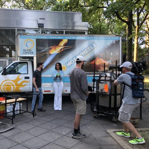 a cameraman recording someone glass blowing and two others talking