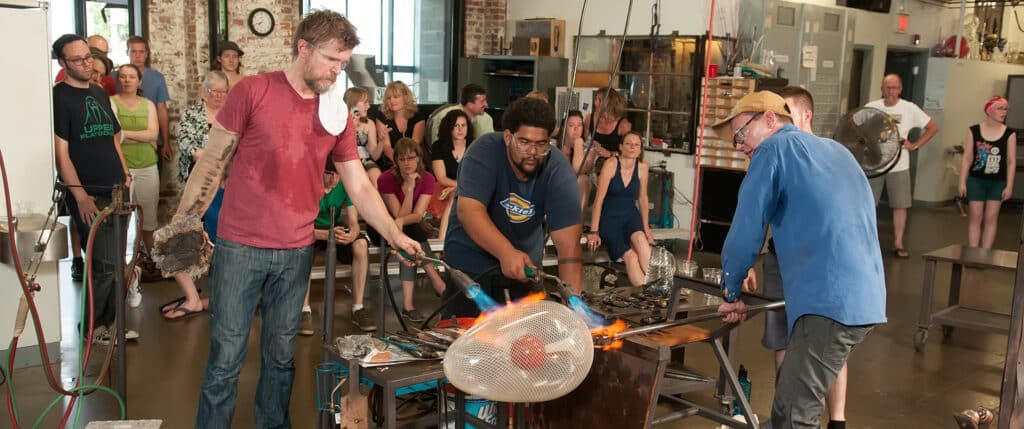 Three men glass blowing in front of an audience