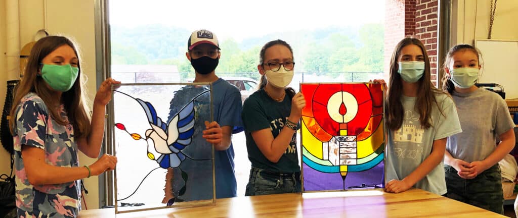 students holding up glass art projects